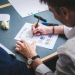 A designer sketches a mobile app prototype on paper at an office desk, focusing on creativity and design.
